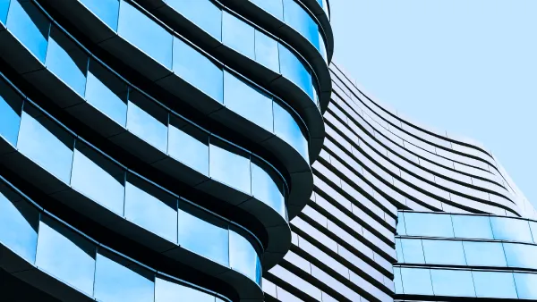 A tall glass building of unusual architecture in a wavy style, against a blue sky