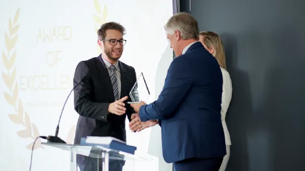 A professionally dressed business man receiving an award from 2 other business people