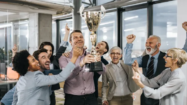 A group of people at a office hoisting a trophy and celebrating