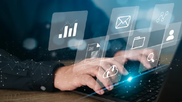 Someone typing on a laptop with a heads up display in the air around him of various computer app icons