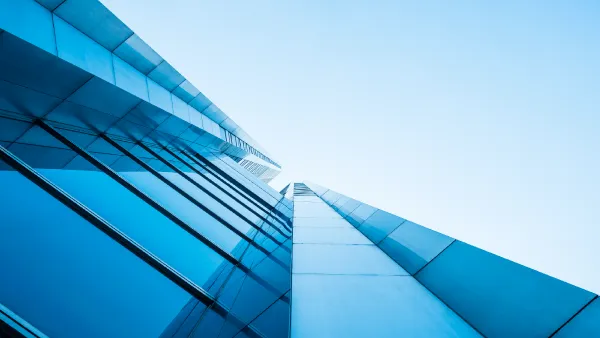 A view looking straight up the side of a very tall high rise glass building into a grey and blue sky