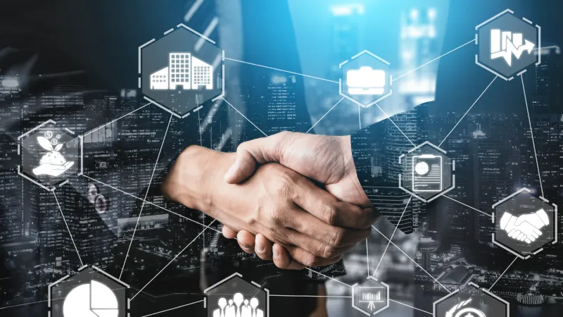 Two business people shaking hands with symbols of business and commerce in light lines floating in front of them