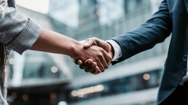 A person in a business suit shaking hands with a person with a casual shirt on