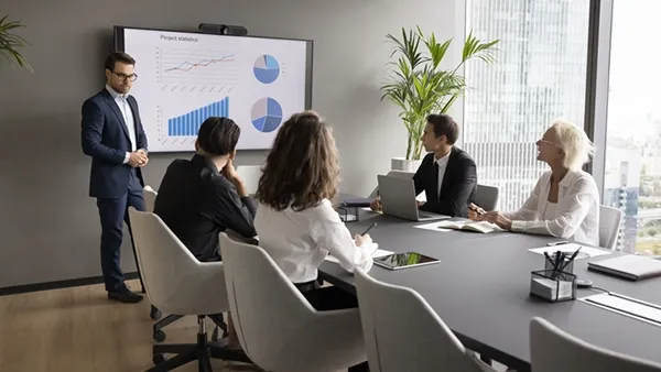 Professional team meeting in a conference room, with a presenter reviewing project charts on a screen.