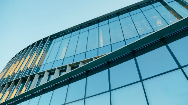 The exterior of a large office building made of steel and glass, looking upward to the top, with the sun reflecting off the windows