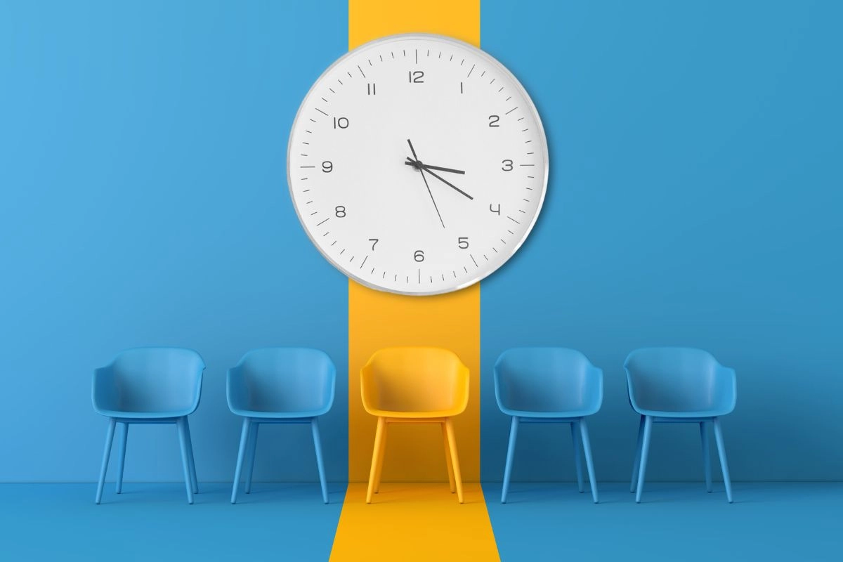 A yellow chair flanked by two blue chairs on each side with a large clock above them